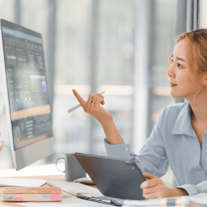 Professional analyzing Power BI dashboard on large screen while working with tablet device, reviewing business analytics and data visualization reports in modern office setting.